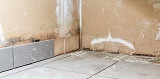 Beschädigte Wand mit dunklen Flecken und entfernten Bodenfliesen